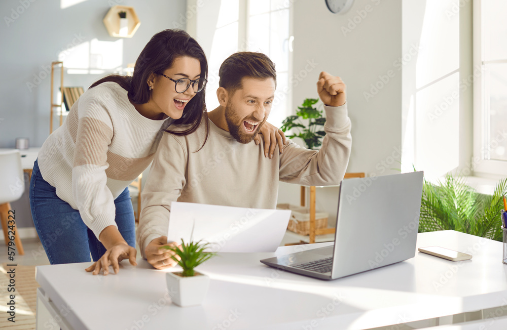Family couple getting excited about success when they get email with excellent job offer. Happy young man and woman reading good news and looking at laptop computer with very excited face expressions Family couple getting excited about success when they get email with excellent job offer. Happy young man and woman reading good news and looking at laptop computer with very excited face expressions