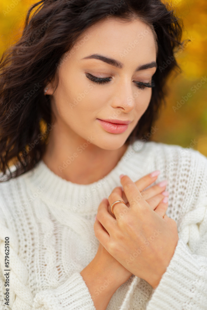 Female outdoors headshot portrait of beautiful young woman with clean beautiful face and skin with curly hair in vintage knitted sweater in autumn park. Hand skin care Female outdoors headshot portrait of beautiful young woman with clean beautiful face and skin with curly hair in vintage knitted sweater in autumn park. Hand skin care