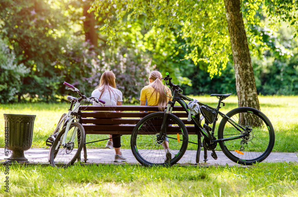 Two bicyclists rest on a Park bench
