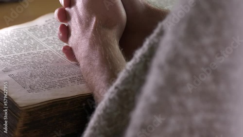 Hands of a Caucasian friar praying over a bible. Back static view