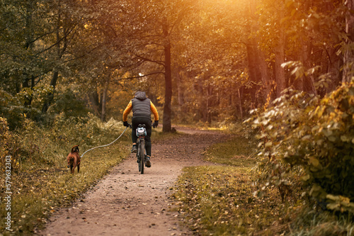 Man rides a bike in the park with his dog