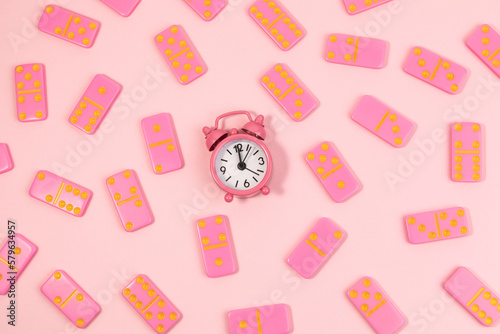 Dominoes and a pink old clock on top view,Pink background.Flat lay