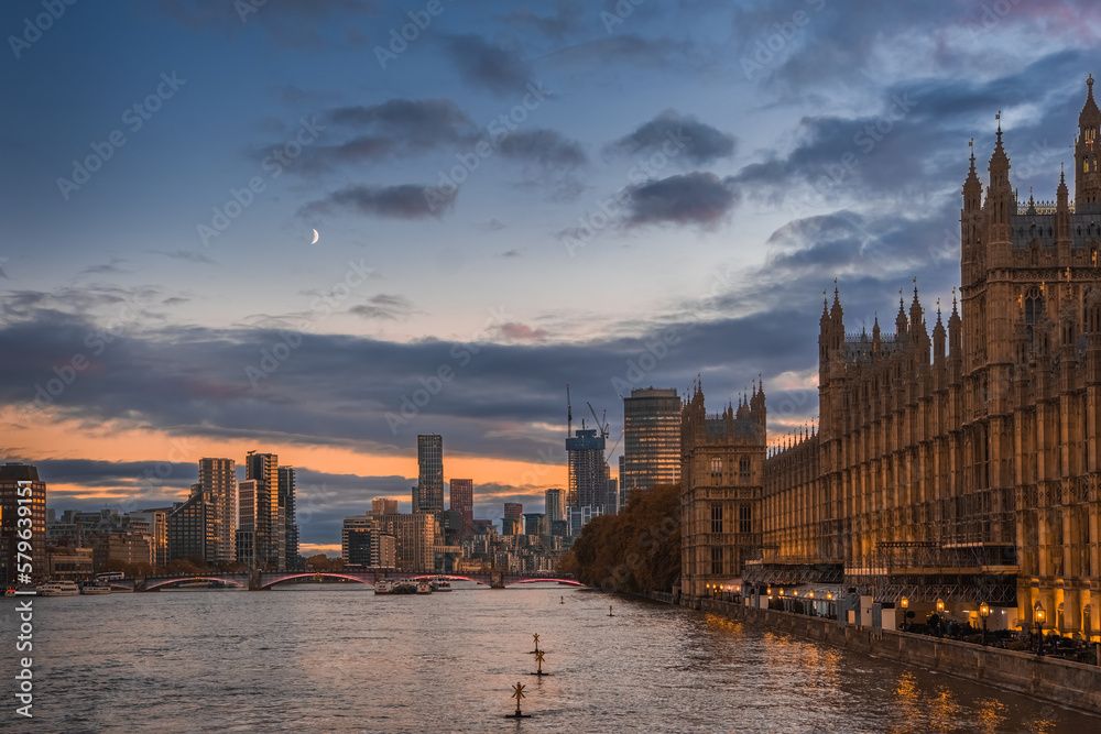 Beautiful  view of Parliament buildings, river Thames and city buildings in London, England,  at sunset with rising moon
