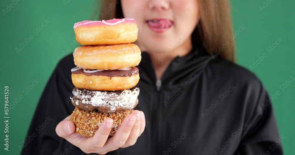 Close up of woman posing isolated over green background choosing between donuts sweeties