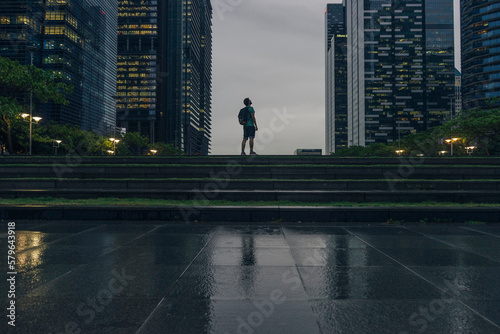 Side view of man with backpack standing on steps in city during rainy season at sunset