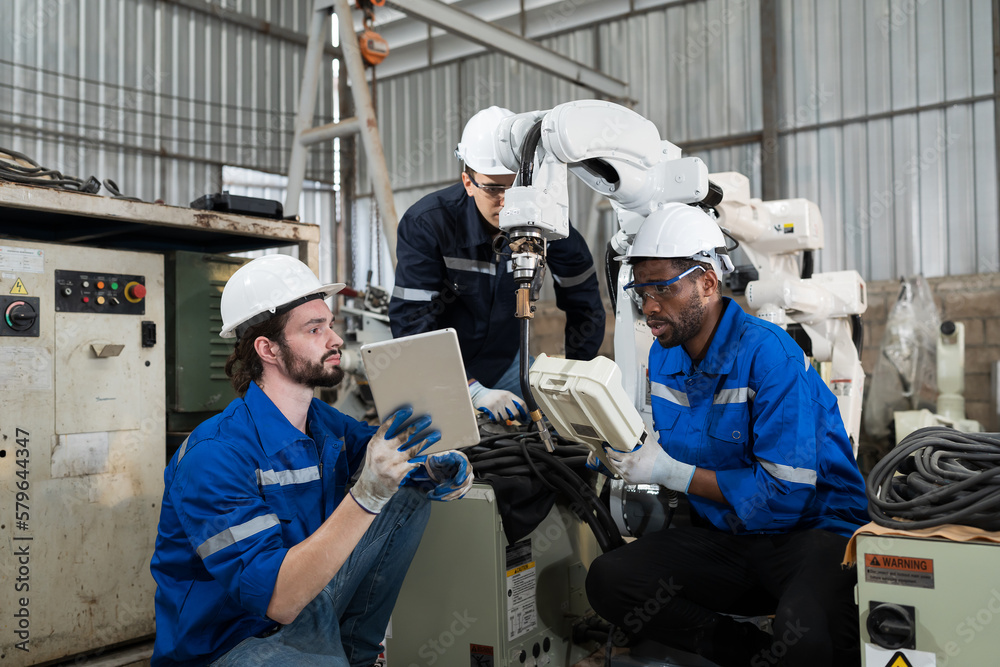 Engineer discuss and control robot arm by remote robot control in workshop. Group of male technician working with control automatic robot arm system welding. Industry robot manufacturing technology Engineer discuss and control robot arm by remote robot control in workshop. Group of male technician working with control automatic robot arm system welding. Industry robot manufacturing technology