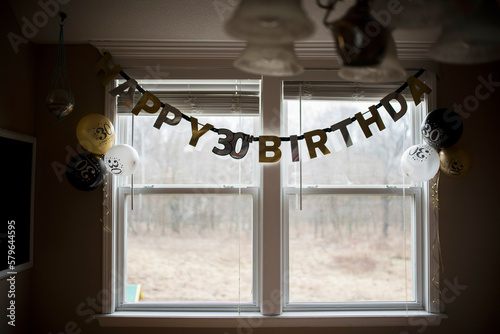 Birthday text on bunting with colorful balloons hanging by window at home photo