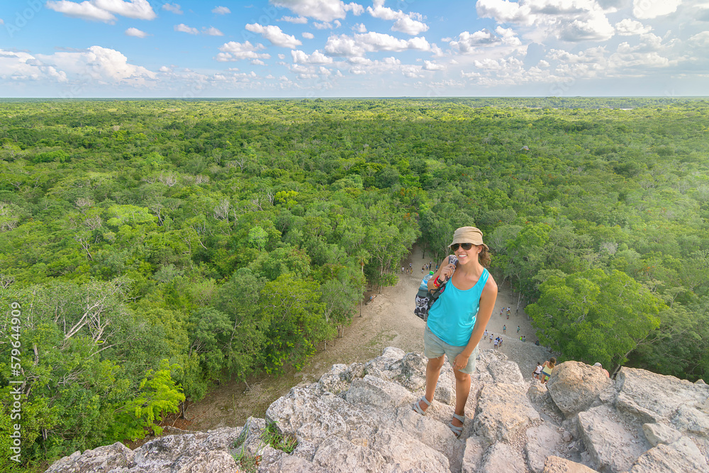 High angle portrait of woman wearing sunglasses and hat while standing on mountain against green landscape