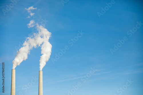 Low angle view of smoke emitting from chimneys against blue sky