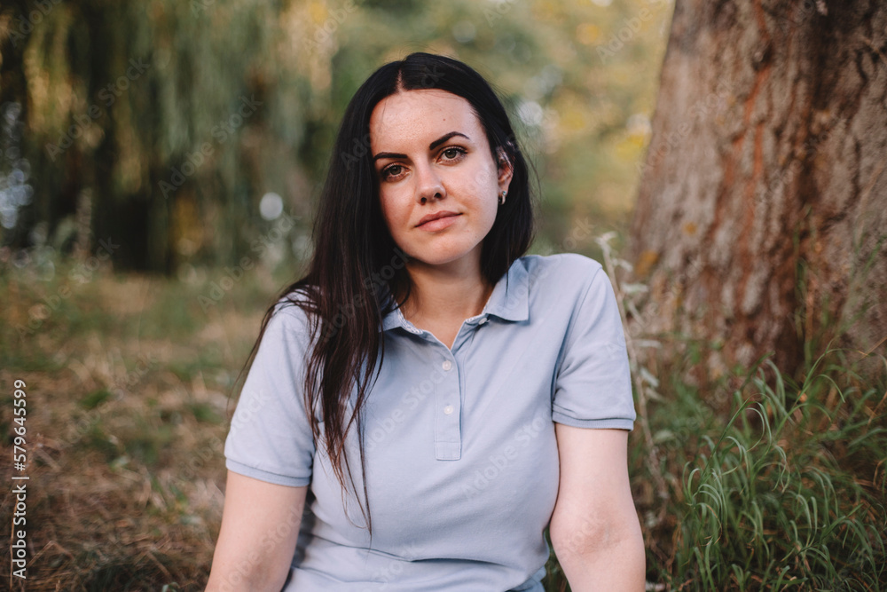 Portrait of serious woman with long hair sitting on field in park Portrait of serious woman with long hair sitting on field in park