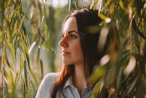 Close-up of thoughtful woman looking away while standing by weeping willow in park
