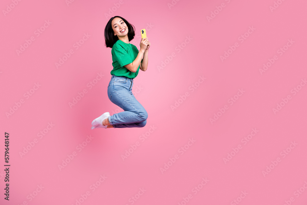 Full body photo of carefree japanese girl jumping energetic hold her new samsung phone enjoy using modern device isolated on pink color background Full body photo of carefree japanese girl jumping energetic hold her new samsung phone enjoy using modern device isolated on pink color background