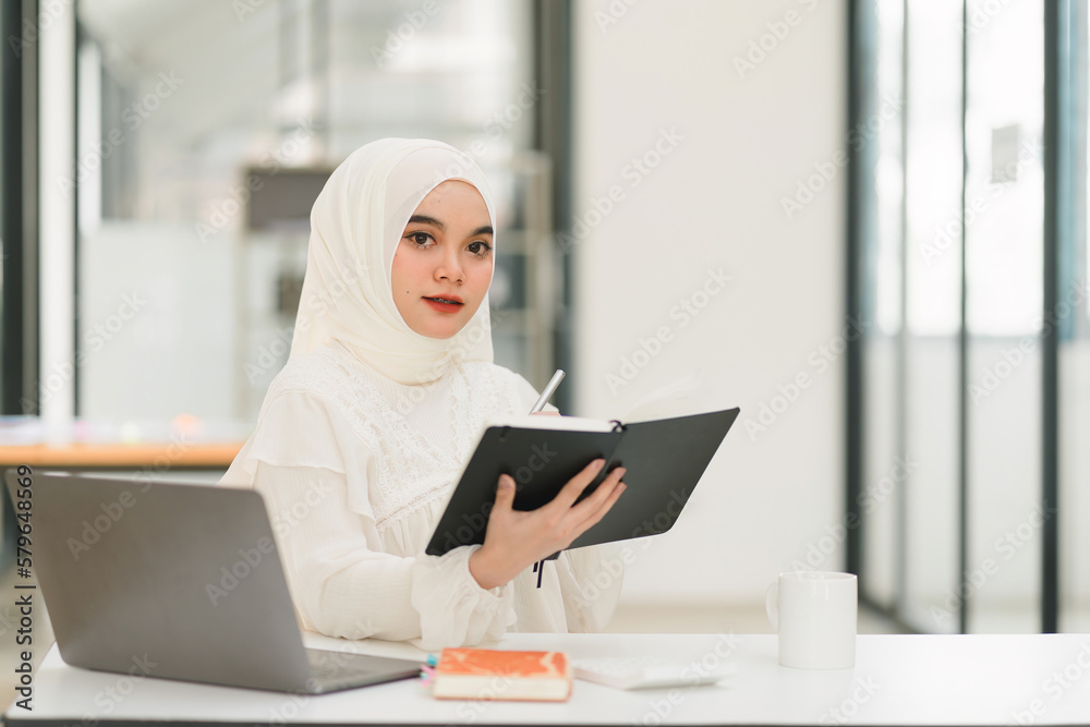 A beautiful Muslim businesswoman is using a digital laptop at her desk in a modern office. A beautiful Muslim businesswoman is using a digital laptop at her desk in a modern office.