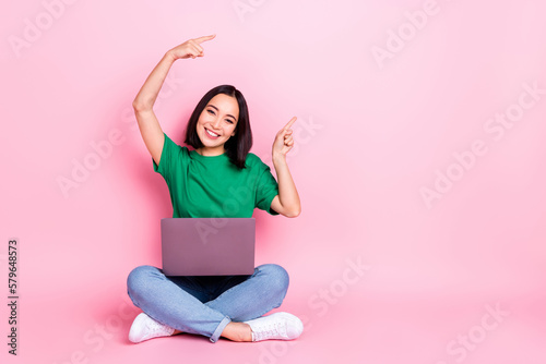 Full size photo of cheerful woman wear oversize t-shirt sitting with laptop indicating empty space isolated on pink color background