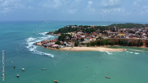 Right trucking aerial drone wide shot of the Cacimba beach in the beach town of Baia Formosa in Rio Grande do Norte, Brazil with fishing boats, coastal houses, small waves, and sea birds flying around photo