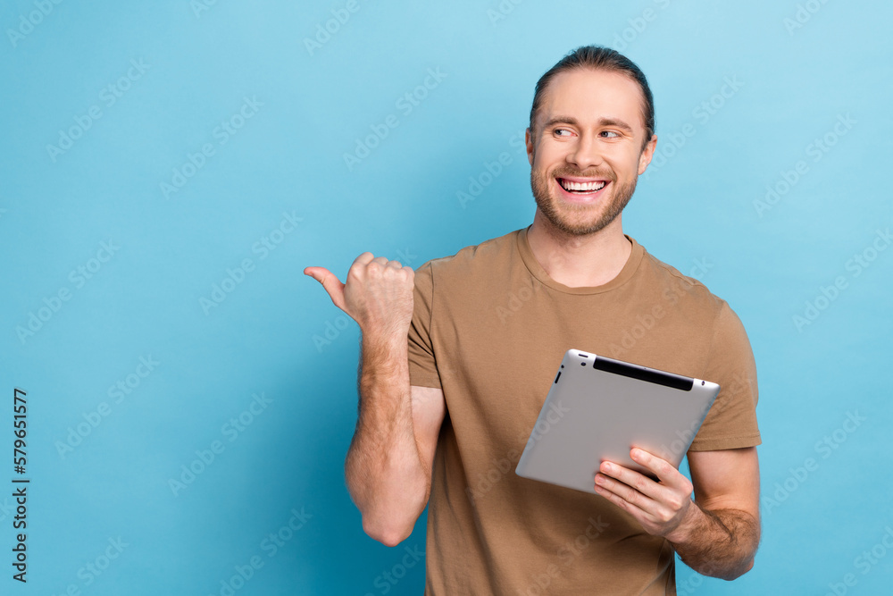 Photo of positive handsome man tail hairdo dressed beige t-shirt directing look empty space hold tablet isolated on blue color background Photo of positive handsome man tail hairdo dressed beige t-shirt directing look empty space hold tablet isolated on blue color background