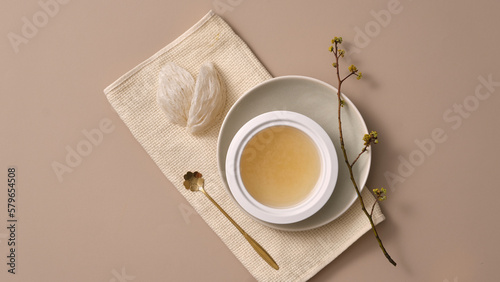 Top view of edible bird’s nest, a golden spoon and white bowl filled with bird’s nest soup, placed on napkin. High-quality dessert well-liked by women in Asia