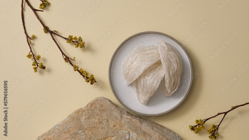 Φωτογραφία Advertising scene for natural island nest product with raw bird’s nest on round dishes, stone and flower branches on beige background