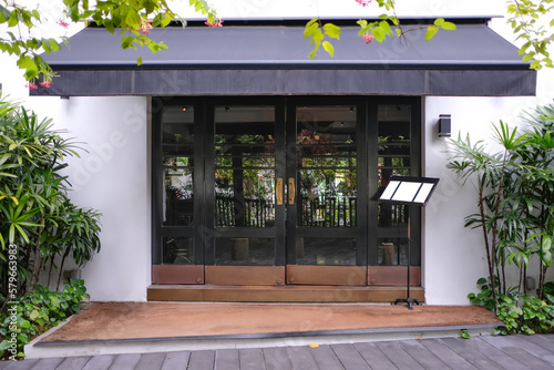 Front view of shop front with awning and framed glass doors. Lush facade of store front design for branding mock up template. Classic exterior for restaurant, cafe or boutique space