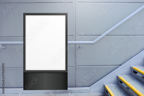 Blank white vertical digital display in front of painted concrete wall, beside flight of stairs. Template for mock up of advertising poster