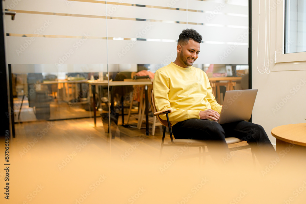 Concentrated determined young freelancer guy sitting in armchair in relaxed pose, typing on laptop, programmer is working on project, developing software, male student websurfing