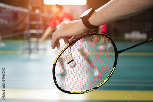 Badminton player holds racket and white cream shuttlecock in front of the net before serving it to another side of the court.  © Sophon_Nawit