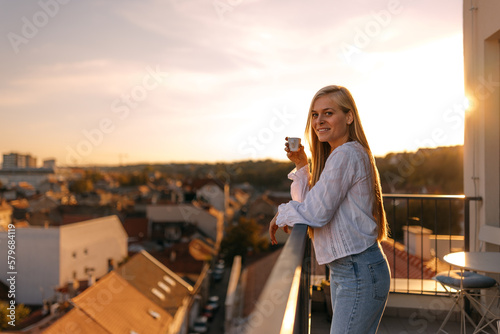 Portrait of a woman with a long blonde hair, holding a cup of coffee, enjoying the sunny day.