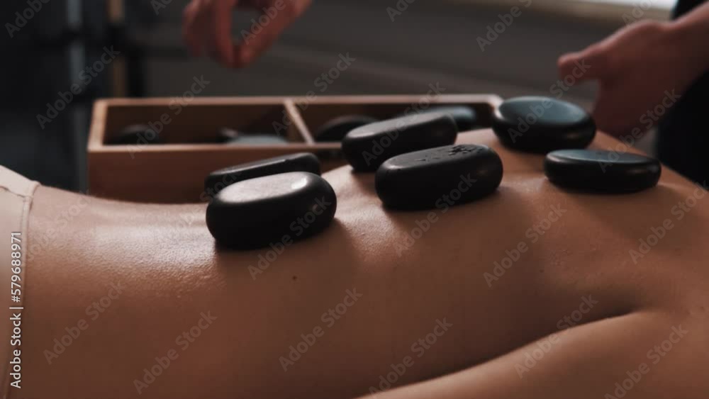Close-up of male hands placing hot black stones on a beautiful woman's back for a special heated massage Close-up of male hands placing hot black stones on a beautiful woman's back for a special heated massage