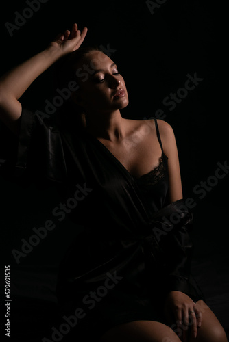 a woman in black nightwear poses in the shadow of a room © dmitriisimakov