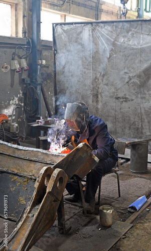 A worker welding metal parts on a construction site. A welder welds parts of a large machine in a metallurgical workshop. An interesting example of manual work. 