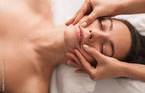 Crop masseuse doing face massage to client