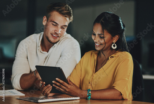 The world online will enable them to beat the deadline. Shot of two businesspeople using a digital tablet together in an office at night.