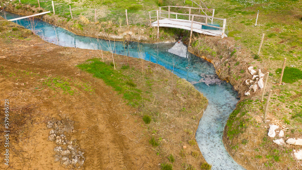 Fototapeta premium Aerial view on a small stream flowing in the middle of the countryside. The river is clear blue and there is nobody on its banks.