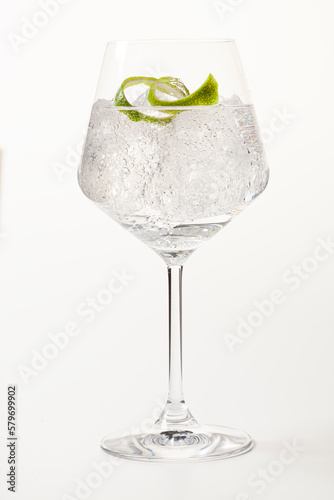 Glass of gin and tonic with lime peel on white background.