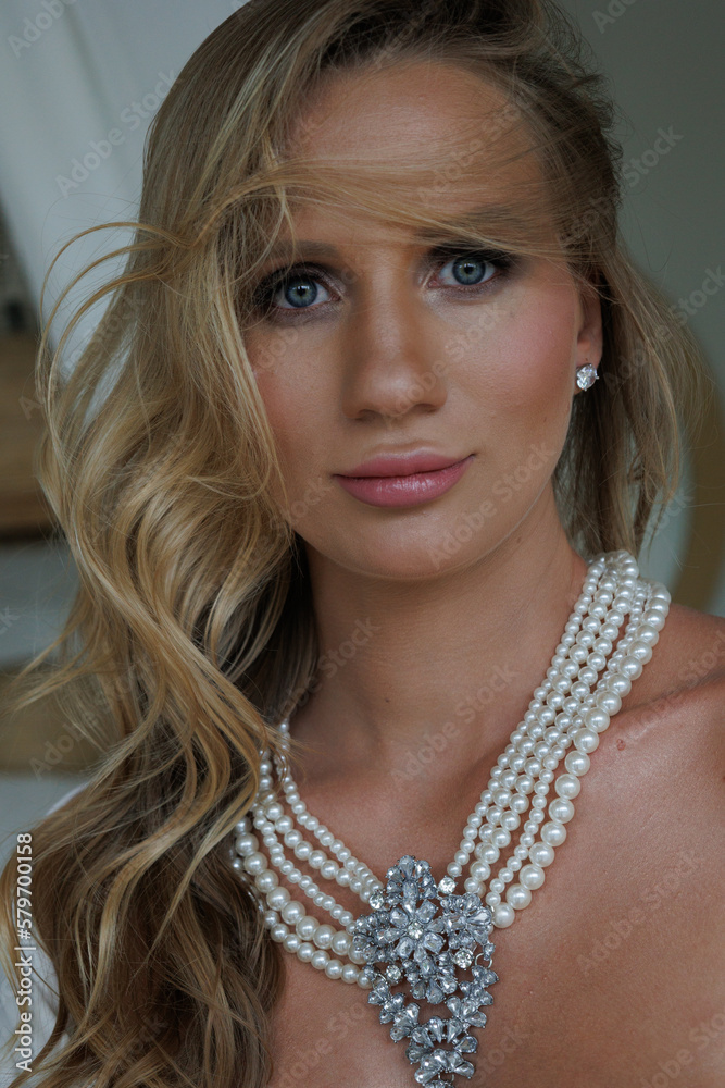 Portrait of beautiful blond woman. Young blond lady in spacious room. Pretty woman with pearl collar waiting child.