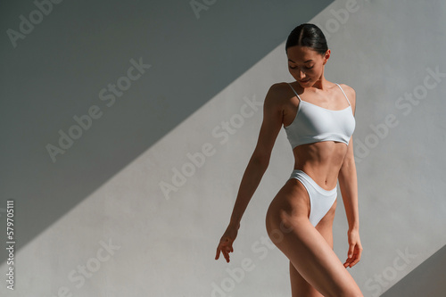 Standing against the wall and showing body. Young caucasian woman is indoors in the studio