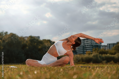Fototapeta Naklejka Na Ścianę i Meble -  Doing stretching yoga exercises. Young caucasian woman with slim body shape is in the fitness clothes outdoors