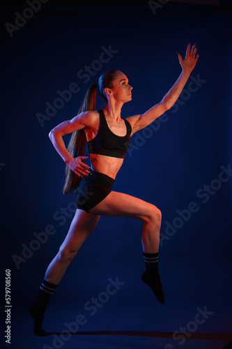 Running, conception of sports. Beautiful muscular woman is indoors in the studio with neon lighting