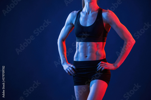 Close up view of abs. Beautiful muscular woman is indoors in the studio with neon lighting
