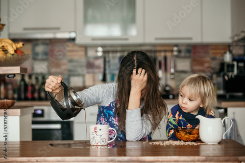 Tired mother, trying to pour coffee in the morning. Woman lying on kitchen table after sleepless night photo