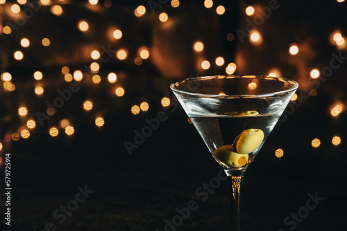 A glass of Dry martini with two olives, with blurred background light, and bokeh on a night club bar counter