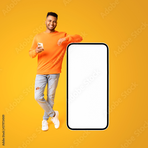 Obraz na płótnie Handsome indian man standing near huge smartphone with empty blank screen, smili