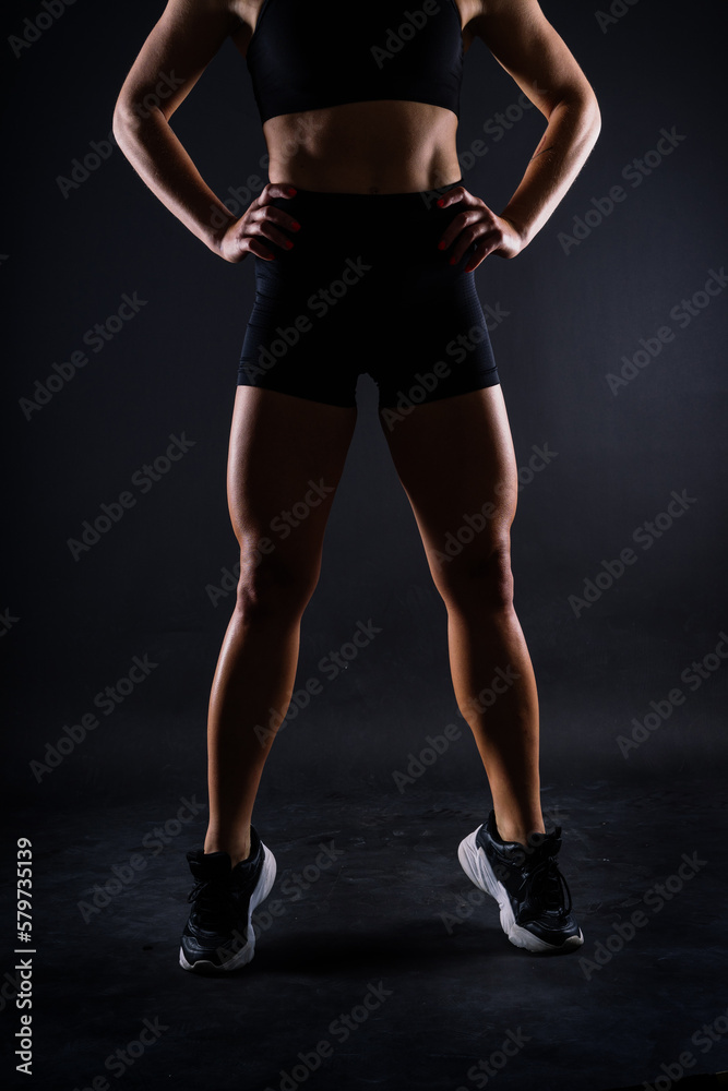 Shaped female legs in sneakers sculpted in muscles, dark background Shaped female legs in sneakers sculpted in muscles, dark background