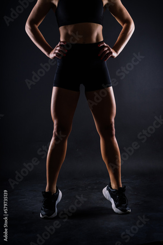 Shaped female legs in sneakers sculpted in muscles, dark background