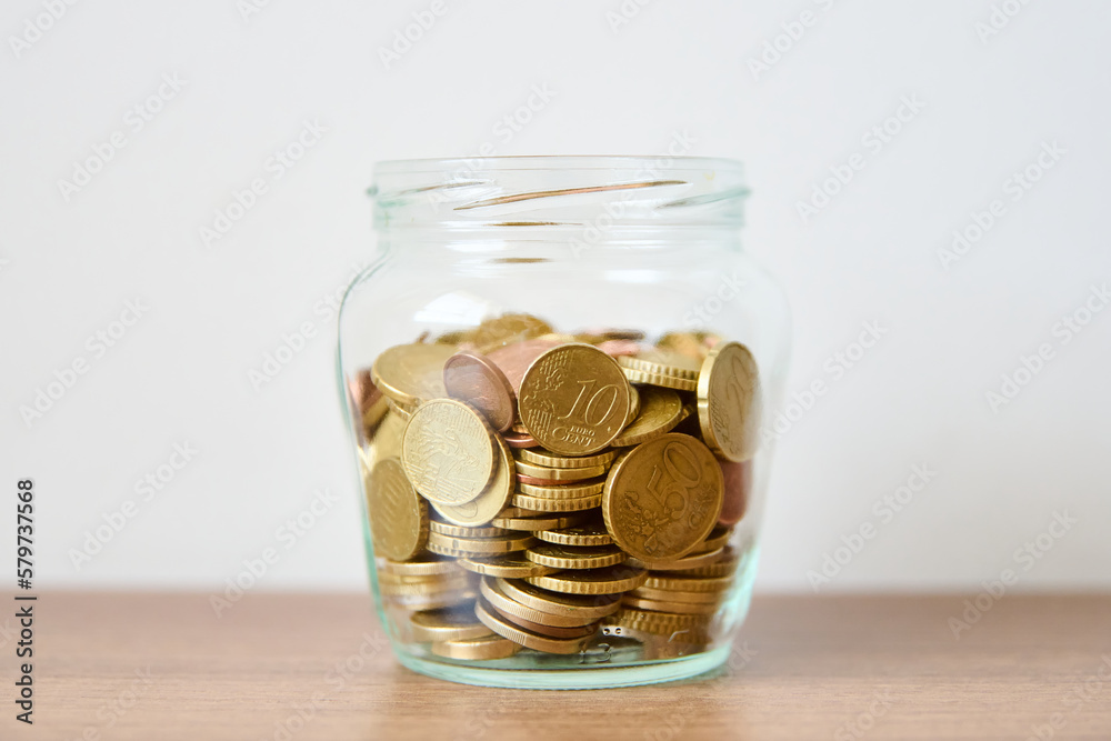Coins in glass jar on wooden table and white wall background. Coins in glass jar on wooden table and white wall background.
