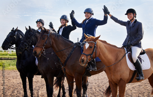 We did it. Cropped shot of a group of attractive young female jockeys high-fiving while sitting on their horses backs.