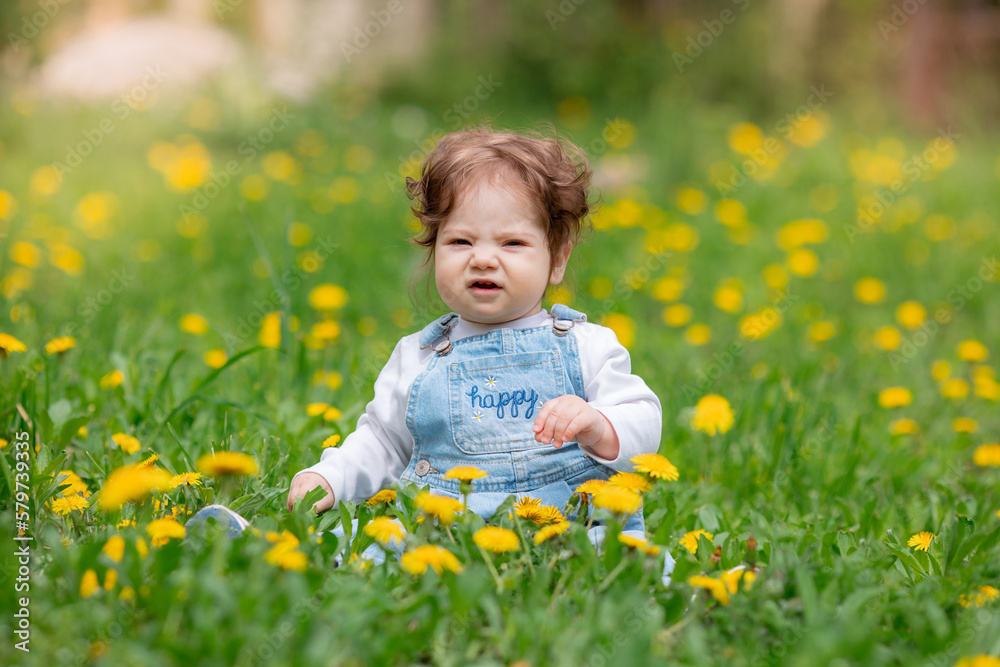 Happy little baby girl sitting on a green meadow with yellow flowers dandelions on the nature in the park Happy little baby girl sitting on a green meadow with yellow flowers dandelions on the nature in the park