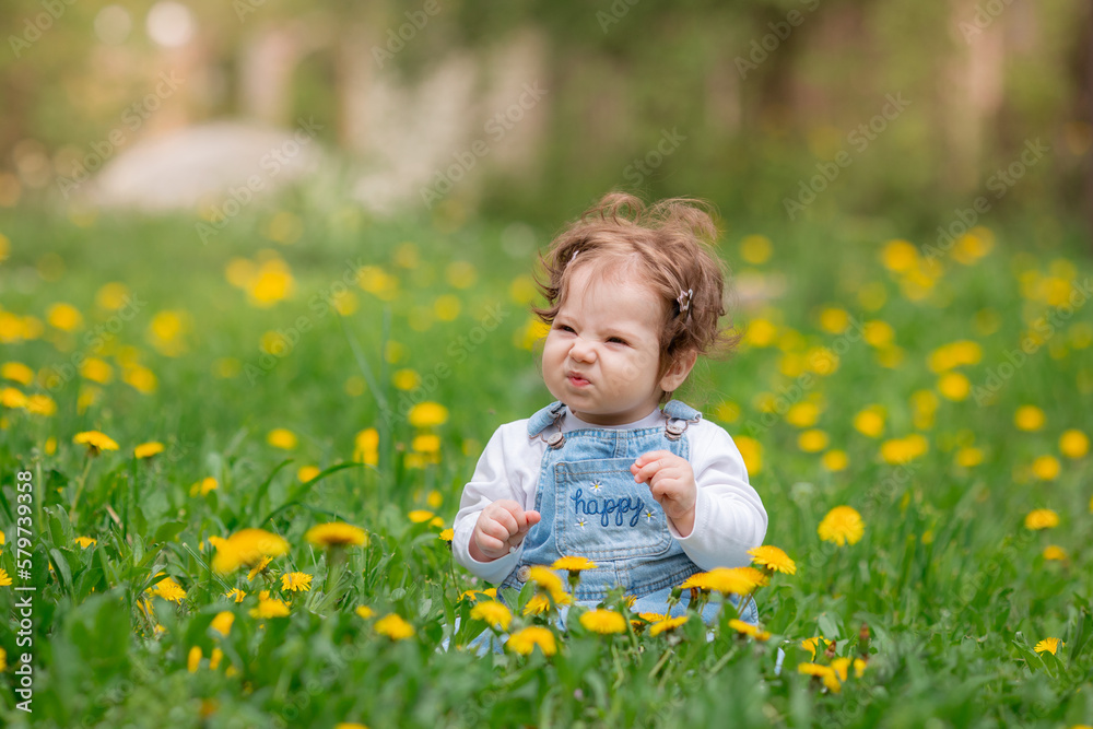 Happy little baby girl sitting on a green meadow with yellow flowers dandelions on the nature in the park Happy little baby girl sitting on a green meadow with yellow flowers dandelions on the nature in the park