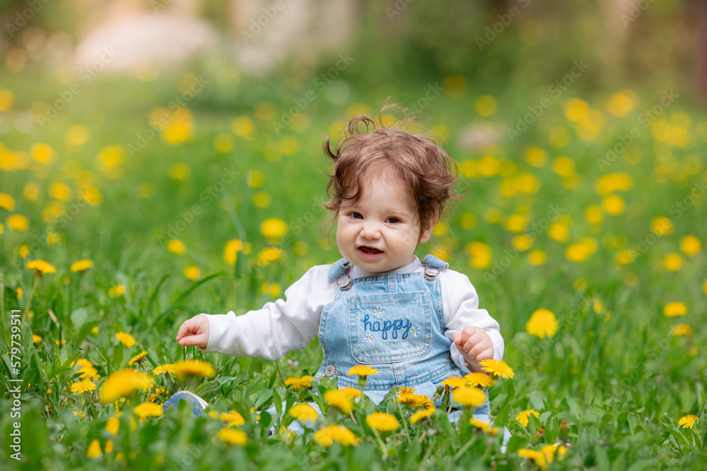 Happy little baby girl sitting on a green meadow with yellow flowers dandelions on the nature in the park Happy little baby girl sitting on a green meadow with yellow flowers dandelions on the nature in the park