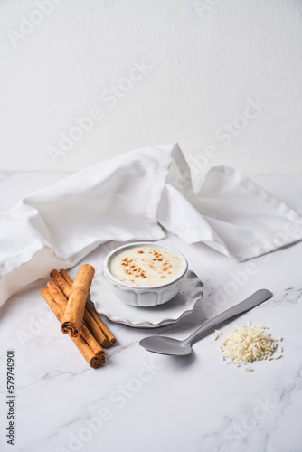 Creamy rice pudding or arroz con leche topped with cinnamon on a white marble background